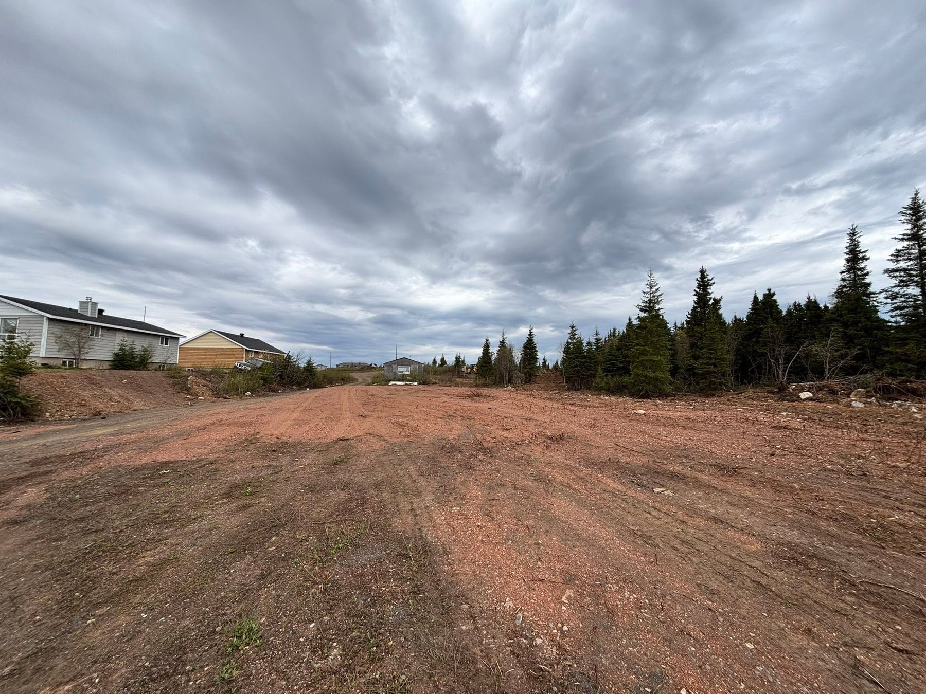 Cleared red-earth area near homes and forest.